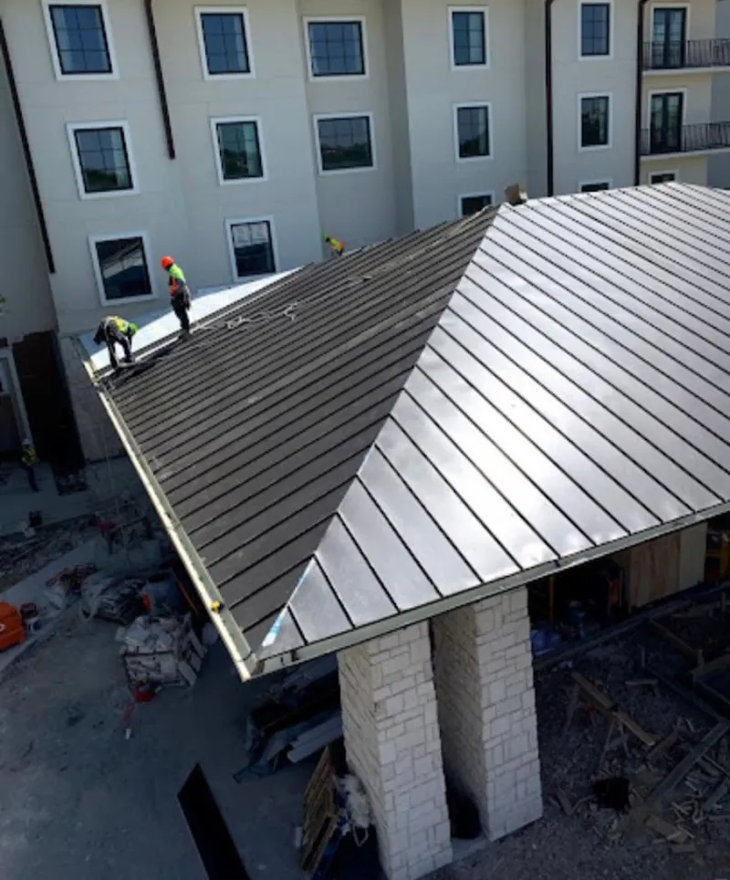 Crew installing standing seam metal roof panels on a commercial project in De Witt